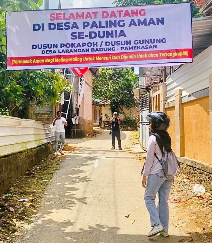 SINDIRAN: Warga melintas di bawah banner di Dusun Pokapoh, Desa Larangan Badung, Kecamatan Palengaan, Pamekasan, Kamis (21/8). (MOH. IQBAL AFGANI/JPRM)