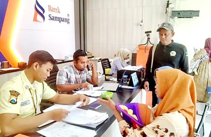 TERTIB: Petugas mendampingi penerima saat mengurus pencairan bantuan disabilitas di Kantor Bank Sampang, Senin (11/8). (JUNAIDI PONDIYANTO/JPRM)
