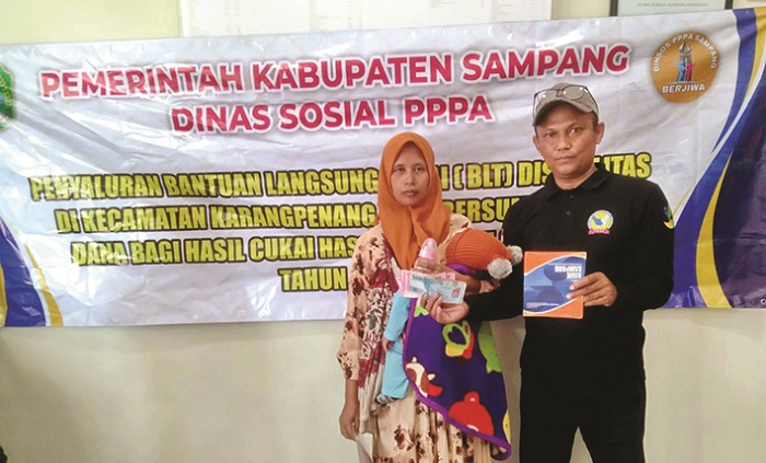 SENANG: Penerima bantuan dari Kecamatan Karang Penang dibantu petugas menunjukkan uang bantuan yang diterima, Senin (11/8). (DINSOS PPA UNTUK JPRM)