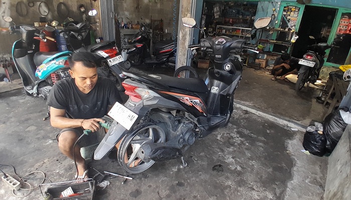 KERJA KERAS: Mawes, karyawan bengkel otomotif sedang memperbaiki roda kendaraan di Jalan RE Martadinata, Bangkalan, beberapa waktu lalu. (M. KHOLIL RAMLI/JPRM)