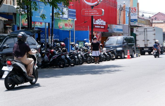 RAWAN BOCOR: Jukir mengawal pengendara di Jalan Panglima Sudirman Bangkalan.&nbsp;  (VIVIN AGUSTIN HARTONO/Radarmadura.id)