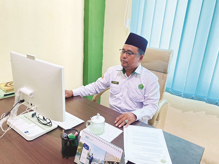 SANTAI: Kepala Kantor Kemenhaj Sampang Sayfuddin melihat data CJH saat ditemui di ruangan kerjanya Selasa (2/12). (AYU LATIFAH/JPRM)
