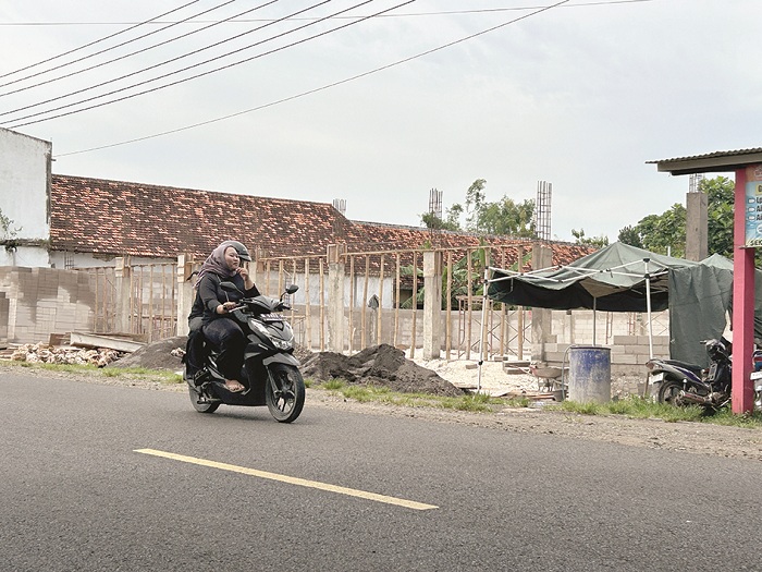 TELAN ANGGARAN JUMBO: Warga berkendara di dekat proyek pembangunan gedung KDMP Desa Keleyan, Kecamatan Socah, Bangkalan, Kamis (8/1). (VIVIN AGUSTIN HARTONO/JPRM)