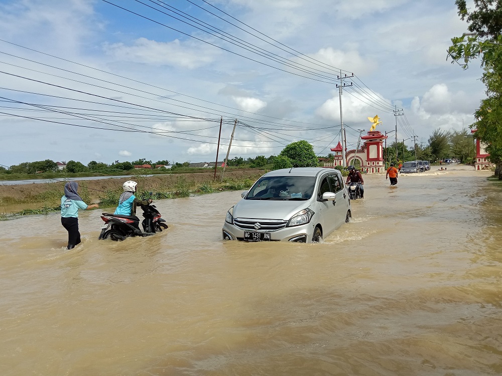 TERGENANG: Masyarakat mendorong kendaraannya di Jalan Nasional Sumenep&ndash;Pamekasan di Desa Nambakor, Kecamatan Saronggi.