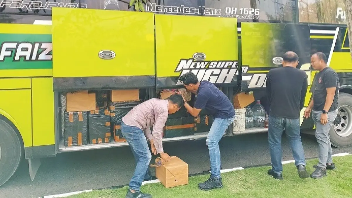 ILEGAL: Polisi mengecek BB rokok ilegal di dalam bagasi bus yang berhasil diamankan di halaman Polres Sampang, Selasa (23/12/2025). (UBAIDILLAHIR RA’IE/JPRM)