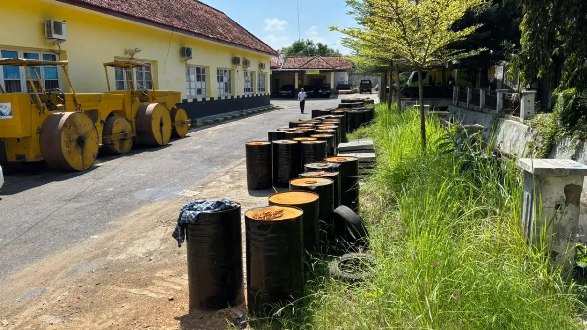 BELUM DISALURKAN: Warga berada dekat drum berisi aspal yang berada halaman Dinas PUPR Pamekasan, Rabu (3/6).
