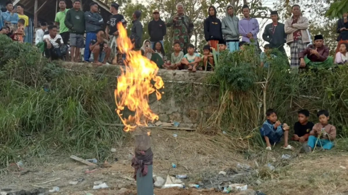 BERKOBAR: Warga sedang berada di sekitar sumur bor yang mengeluarkan api di Desa Karang Gayam, Kecamatan Omben, Sampang, Senin (6/7). (ISTIMEWA)