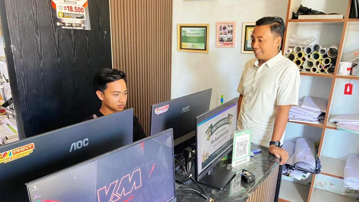 SANTAI: Lutfiadi mengecek desain banner di toko miliknya di Jalan Dirgahayu Pamekasan Selasa (14/7).