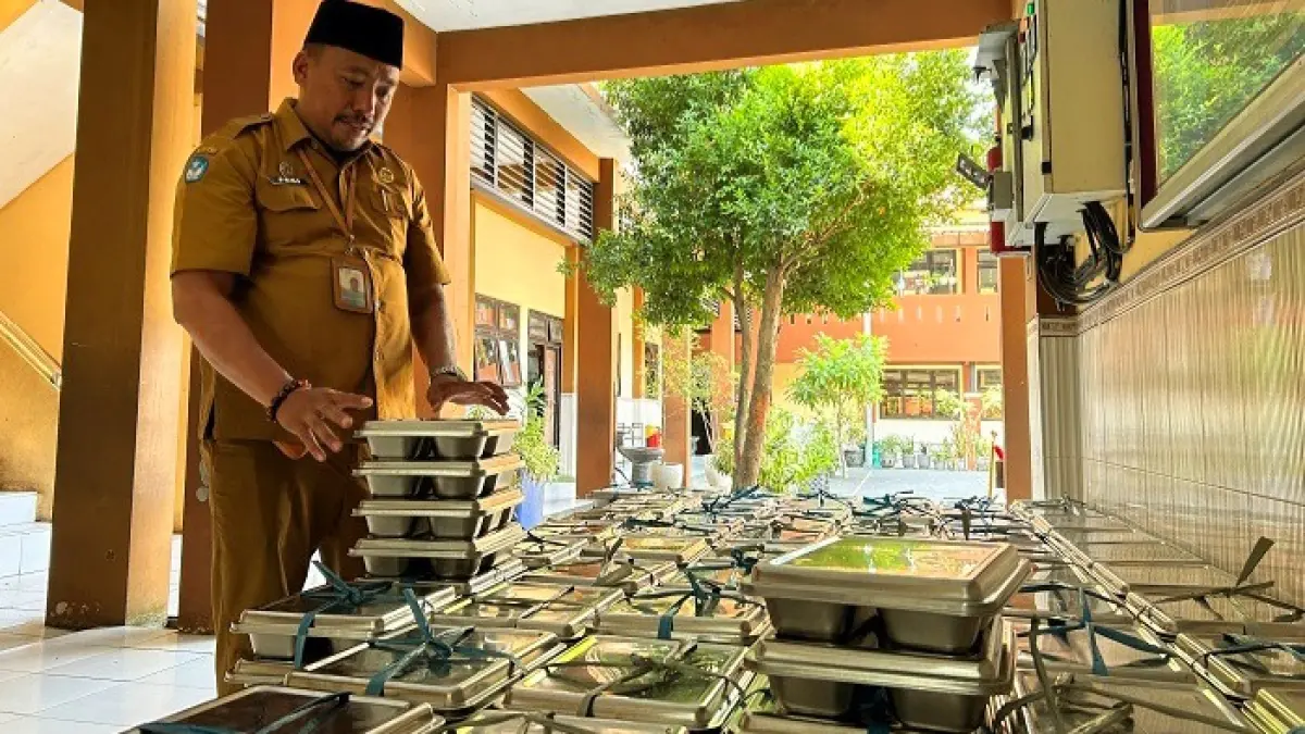 TELITI: Guru SDN Kemayoran 1 Bangkalan Feri Arianto mengecek ompreng MBG sebelum dikembalikan, Senin (13/7). (VIVIN AGUSTIN HARTONO/JPRM)