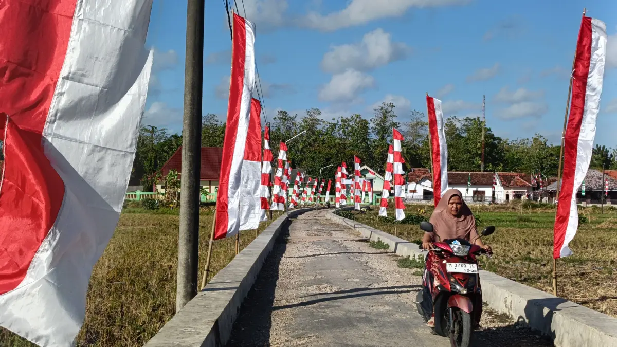 MERAH PUTIH: Seorang warga melintas di jalan utama Pocang Temor yang dipenuhi umbul-umbul merah putih.