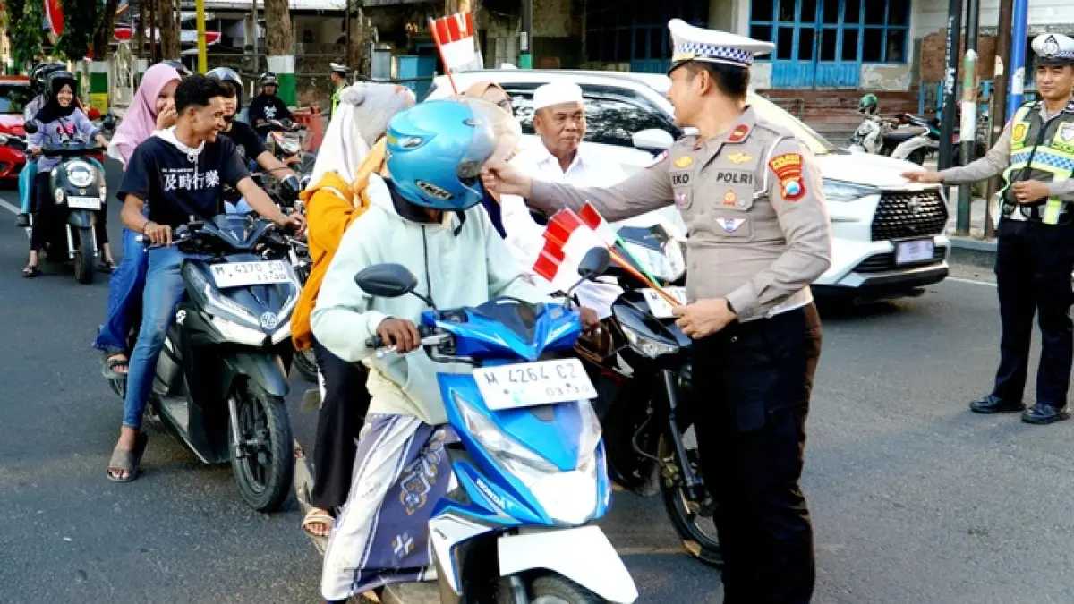 SEMANGAT KEMERDEKAAN: Polisi membagikan bendera Merah Putih kepada pengguna jalan Minggu (16/8). (POLRES PAMEKASAN UNTUK JPRM)