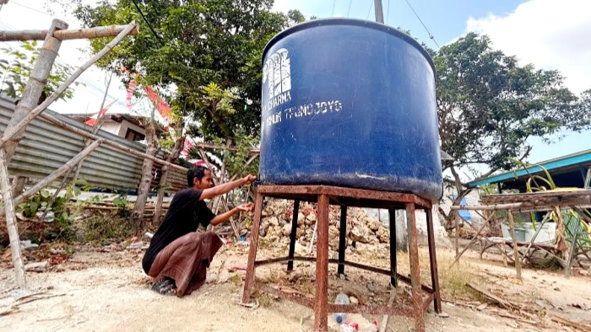 TIDAK MENGALIR: Musleh, warga Desa Baruh, Kecamatan Sampang, berada di sekitar tandon yang belum diisi air oleh PDAM Trunojoyo Sampang Minggu (16/8). (UBAIDILLAHIR RA’IE/JPRM)