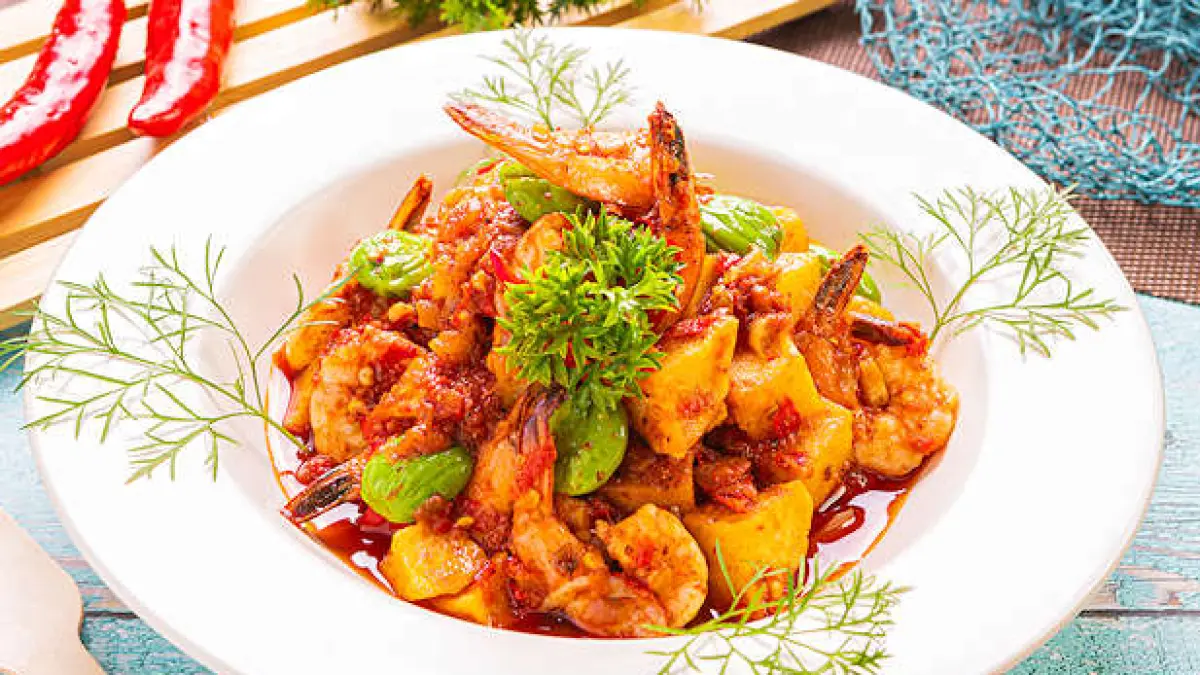 Sebuah hidangan bernama Balado Udang Petai, udang dan petai dengan saus pedas disajikan di piring putih dengan hiasan daun segar.