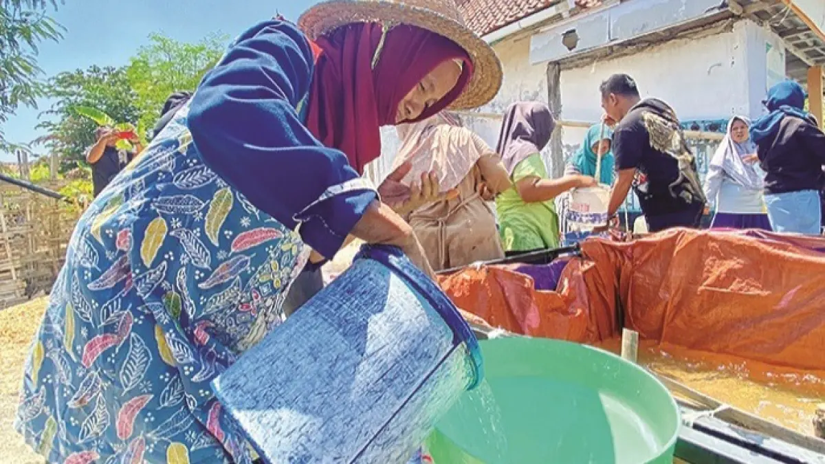 TERIK: Sutiah menuang air bersih ke galon di Desa Larangan Tokol, Kecamatan Tlanakan, Pamekasan, Minggu (6/9). (MOH. IQBAL AFGANI/JPRM)