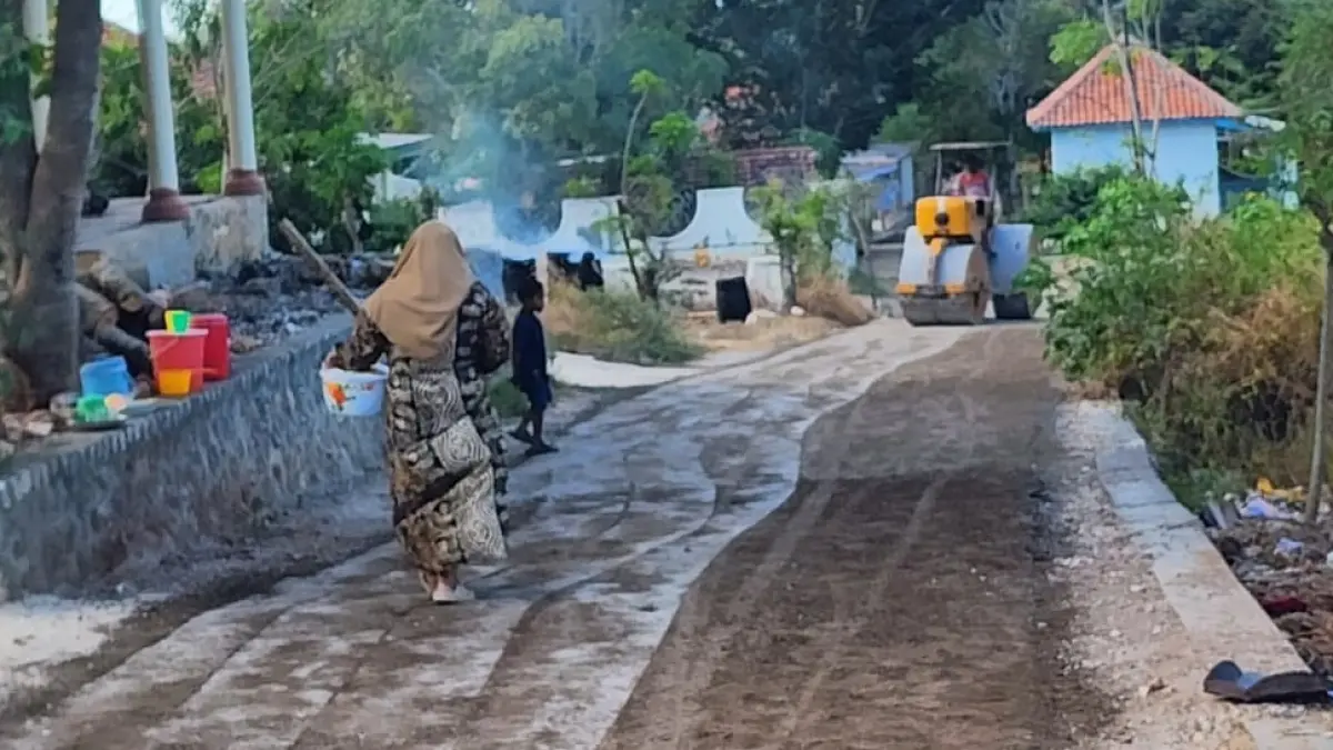 DIKERJAKAN: Warga berada di sekitar pekerjaan pengaspalan jalan di Timur Akses Jalan Poros Desa Dusun Duwek Rajeh, Desa Bira Timur, Kecamatan Sokobanah, Sampang. (PEMDES BIRA TIMUR UNTUK JPRM)