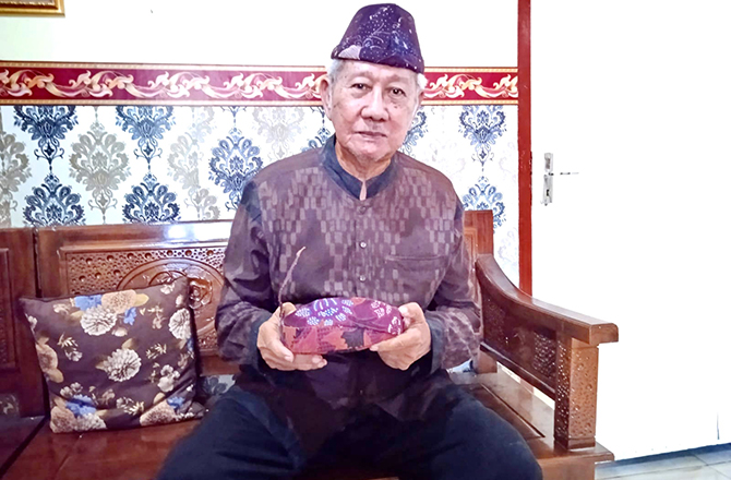 MENJAGA TRADISI: Ketua Peguyuban Kesultanan Bangkalan Abdul Hamid Mustari mengenakan tongkos dan memegang odheng seleredan di kediamannya di Kelurahan Pangeranan, Minggu (17/4). (JUPRI/RadarMadura.id)