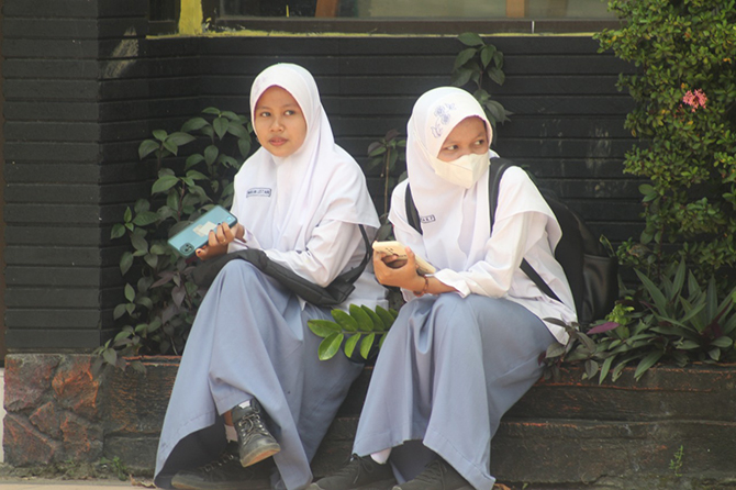 ASYIK NGOBROL: Siswa SMKN 3 Pamekasan duduk santai di sekitar Jalan Kabupaten usai jam pulang sekolah. (MOH. IQBAL AFGANI/RadarMadura.id)