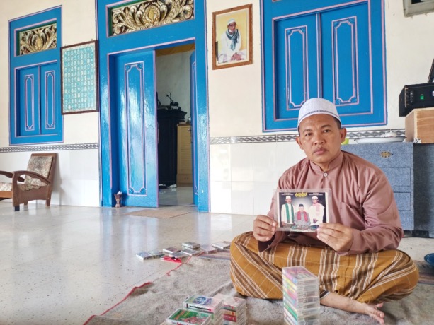 KENANGAN: Mohdar menunjukkan foto Ustad Ahmad Umar bin Ta’lab serta kaset pita yang berisi rekaman hadrah Ahmad Umar bin Ta’lab. (MOH. JUNAIDI/RadarMadura.id)