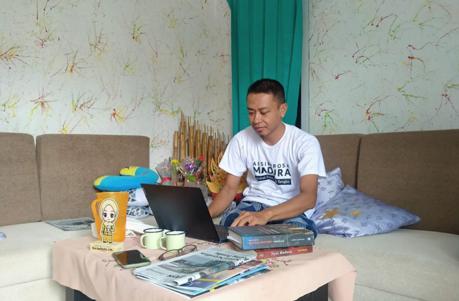 TEKUN: Mudhar menulis cerpen di ruang tamu rumahnya di Perumahan Puri Matahari Blok A Nomor 48, Sampang, kemarin. (FADIL/Radarmadura.id)