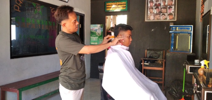 MEMANGKAS: Fathur Rosi melayani pelanggan memangkas rambut di Desa Bilaporah, Kecamatan Socah, Bangkalan, Rabu (19/4). (UBAIDILLAHIR RA’IE/JPRM)