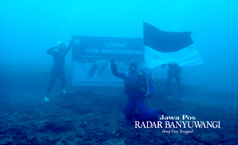 KUATKAN SEMANGAT NASIONALISME: Kasatpolairud Kompol Masyhur Ade bersama anggotanya mengibarkan bendera merah putih dan banner HUT Bhayangkara ke-77 di dasar laut selat Bali, Sabtu (1/7).