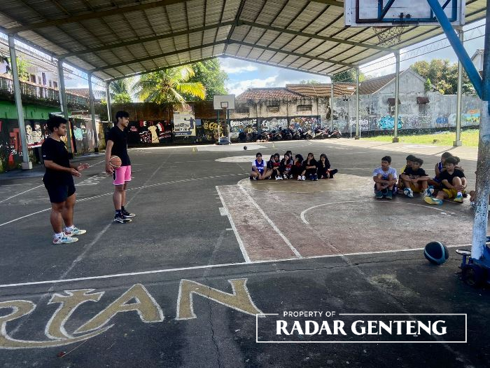 BERIKAN ILMU: Aven (pegang bola) saat melatih basket kepada anak-anak kecil di Lapangan Basket Dusun Kopen, Desa Genteng Kulon, Kecamatan Genteng pada Selasa (4/7)