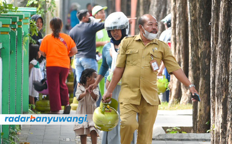 BANTU ISTRI: Pria berseragam ASN ikut menenteng tabung elpiji ukuran 3 kg dalam kegiatan operasi pasar murah di depan Gedung Juang 45 Banyuwangi, Senin (24/7).