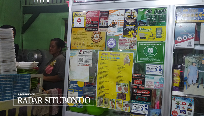 PERANG HARGA: Ragam stiker jasa ojol ditempel di salah satu warung milik pedagang di Situbondo.
