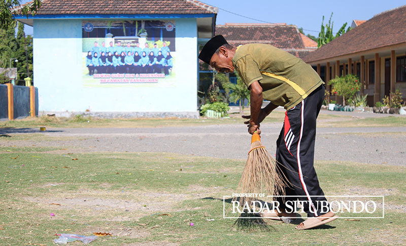 BERSIH-BERSIH: Suparto menyapu halaman sekolah SDN 3 Kilensari, Kecamatan Panarukan, Minggu (27/8).