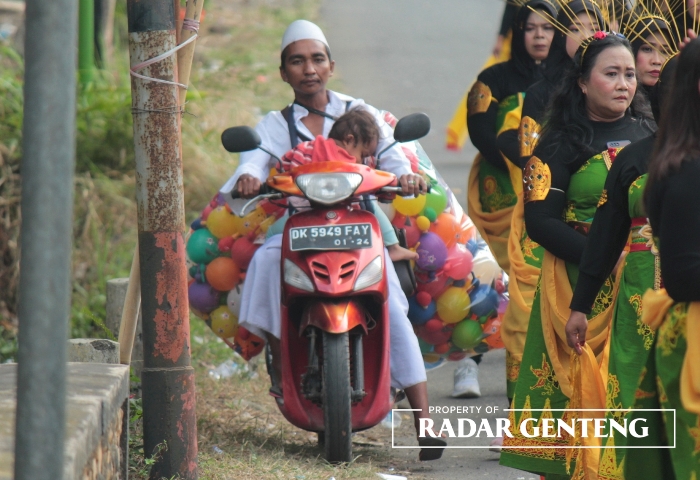 MELINTAS: Saiful membawa barang dagangan sambil menggendong anaknya menerobos barisan karnaval di Desa/Kecamatan Sempu pada Minggu (27/8)