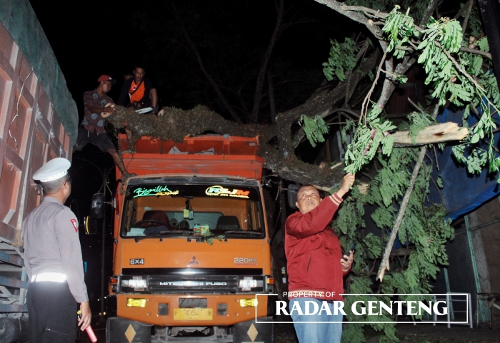 MACET: Kanit Lantas Polsek Genteng, Iptu Nanang Wardhana (kanan) bersama warga dan relawan TRC BPBD mengevakuasi pohon trembesi yang ambruk menimpa truk dan warung yang ada di pinggir jalan raya Desa