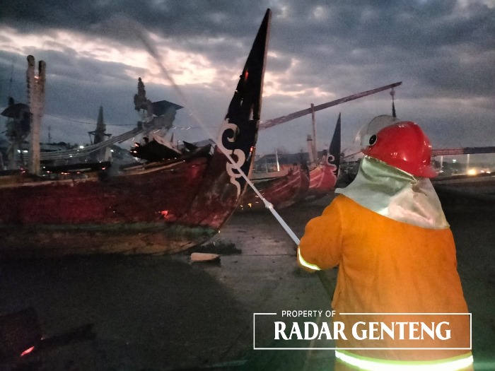 DIPADAMKAN: Petugas Damkar Sektor Srono memadamkan api yang melalap badan kapal gardan di Dermaga Ujung Pelabuhan Muncar, Senin (11/9) petang.