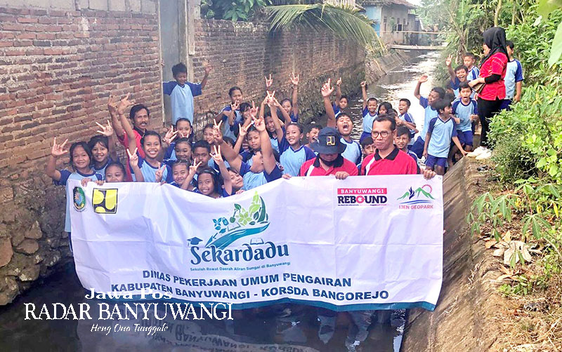 PEGANG BANNER: Siswa dan Korsda Bangorejo dan siswa SDN 6 Kebondalem dalam program Sekardadu di Saluran Sekunder Kebondalem, Kecamatan Bangorejo, Jumat (22/9).
