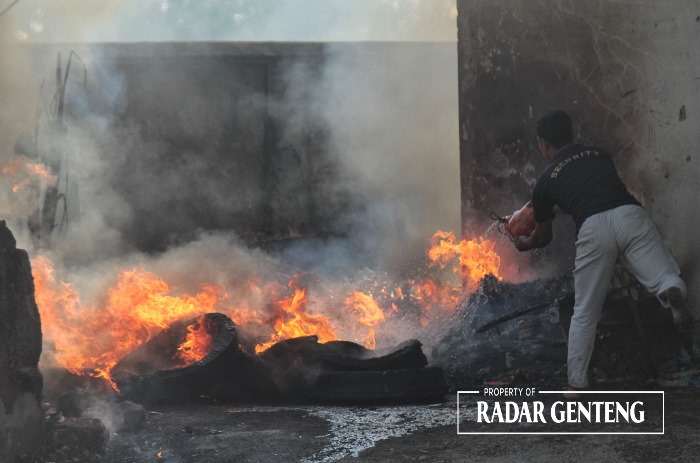MENYALA: Salah satu petugas keamanan, Ahmat Nur Aini memadamkan api yang membakar ban bekas di Gudang OT, Jalan KH Hasyim Asyari, Desa Genteng Wetan, Kecamatan Genteng dengan timba, Minggu (22/10).