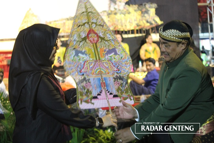 MULAI PAGELARAN: Bupati Ipuk Fiestiendani (kiri) menyerahkan gunungan pada Ki Ghaib Siswoyo (kanan) di RTH Desa Karetan, Kecamatan Purwoharjo pada Selasa (7/11) malam.