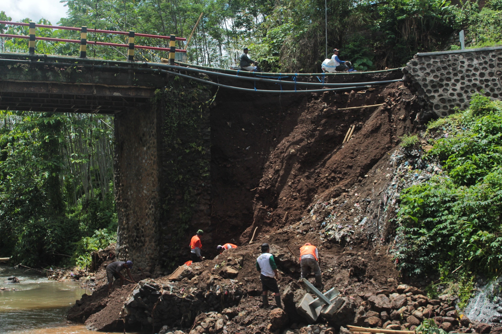 TAHAP AWAL: Pekerja membersihkan puing-puing reruntuhan bangunan plengsengan Jembatan Jagalan yang ambrodi Kampung Madiunan, Dusun Sepanjang Wetan, Desa Sepanjang, Kecamatan Glenmore pada Sabtu (2/12)
