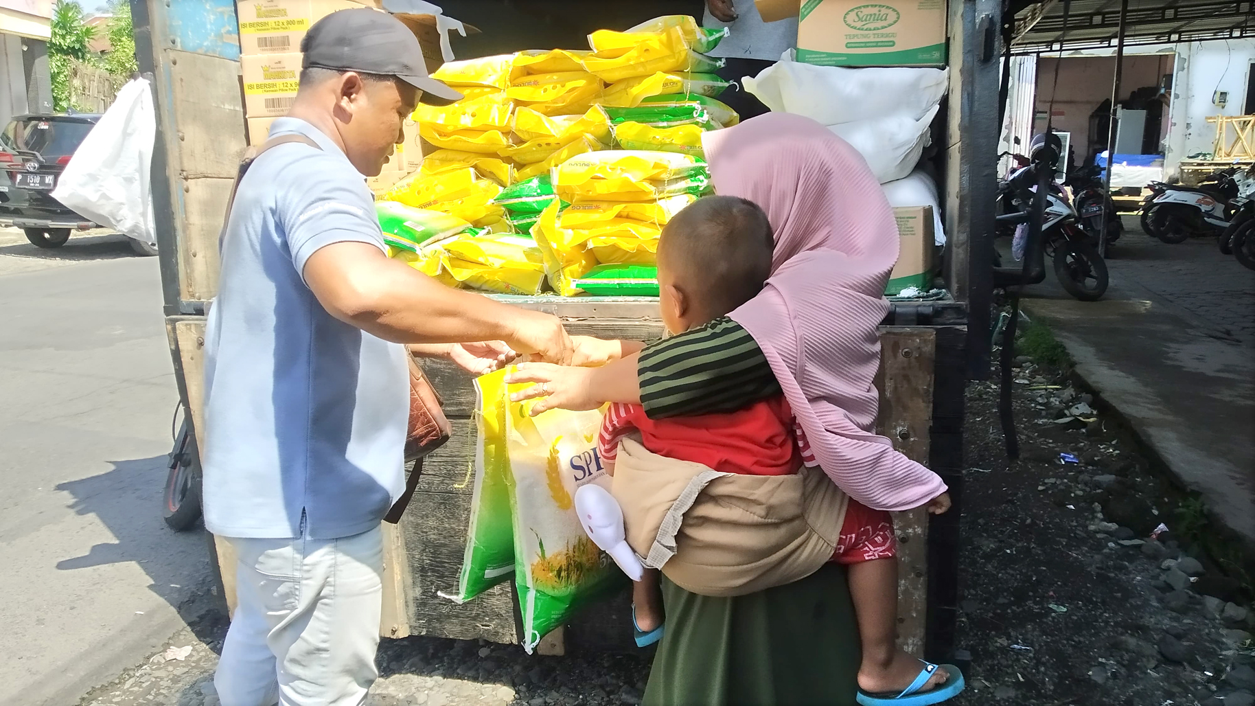 DEMI BERAS: Salah satu ibu sambil menggendong anak mengambil beras dan gula dalam operasi pasar murah di Pasar Sempu Rabu (21/2).