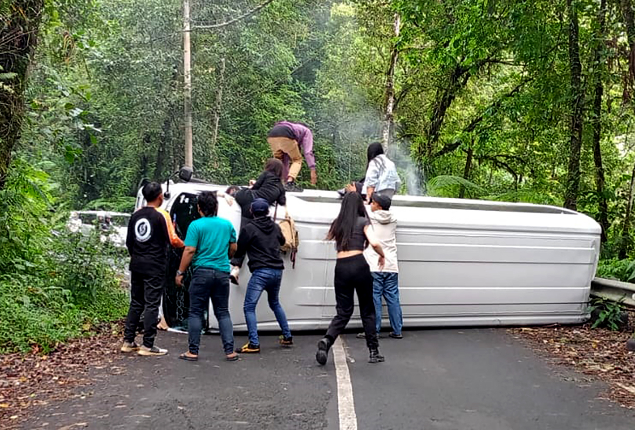 MENUTUP BADAN JALAN: Kondisi mobil Izusu Elf bernopol L 7033 PRK yang mengangkut 15 wisatawan asal Tiongkok terguling di dekat tikungan tajam Sengkan Mayit Jumat (24/5).