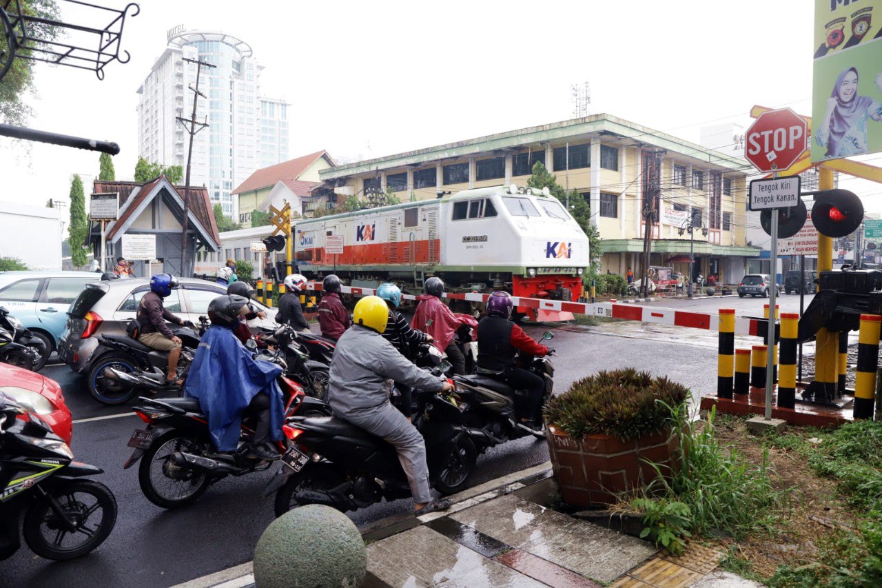 Pengguna jalan menunggu kereta api yang melintas di belakang pintu perlintasan sebidang.