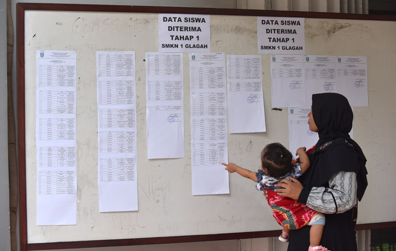 PAPAN PENGUMUMAN: Orang tua siswa dengan menggendong buah hatinya yang masih kecil melihat pengumuman PPDB jalur afirmasi di SMKN 1 Glagah, Jumat &nbsp;(14/6).