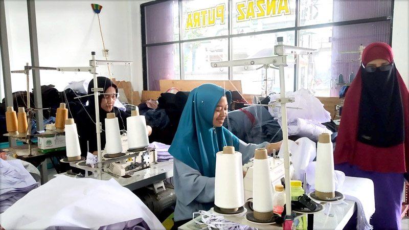 BERTAHAN: Umi Alfiah (kerudung biru) menjahit kain untuk seragam pesanan di Dusun Cangaan, Desa Genteng Wetan, Kecamatan Genteng Selasa (9/7).
