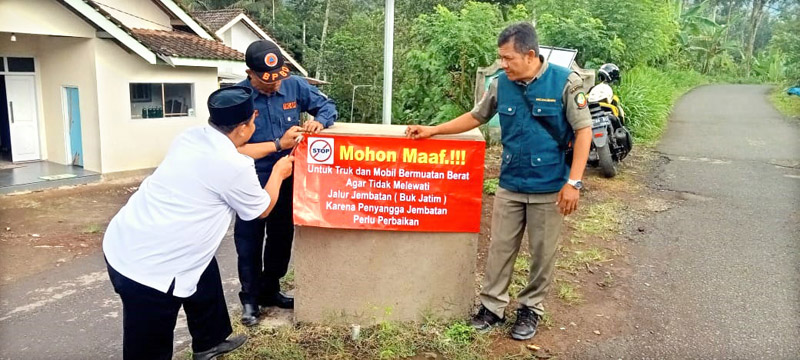 IMBAUAN: Subahrullah (baju putih) memasang papan banner berisi larangan truk muatan berat dilarang melintas di Jembatan Buk Jatim, Desa Banyuanyar, Kecamatan Kalibaru Rabu (10/7).