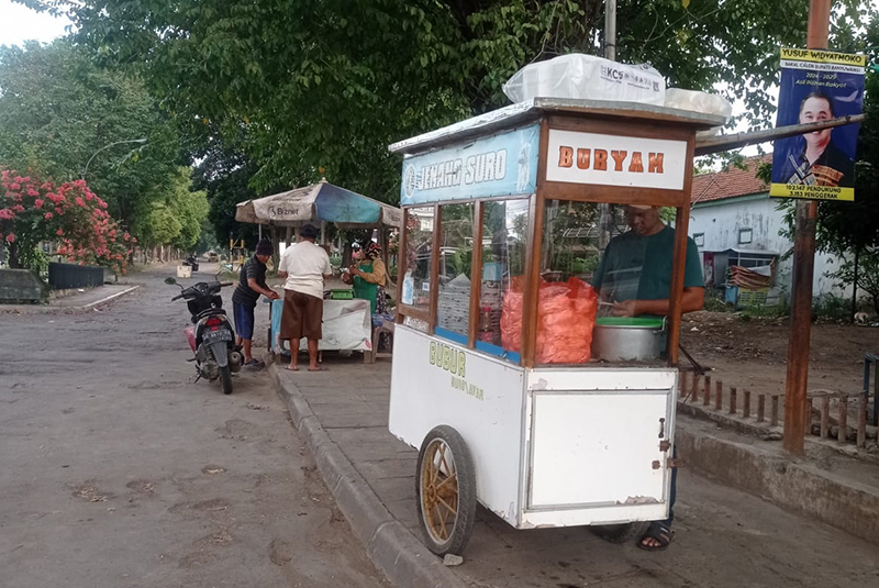 Gerobak bubur ayam jenang syuro bisa dijumpai di pertigaan Jalan Basuki Rahmat Banyuwangi menuju PKBR.