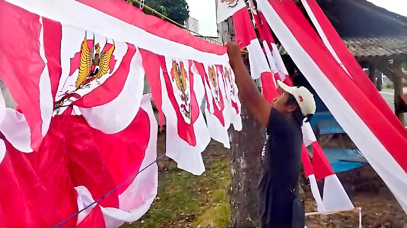 PASANG: Adi Pangestu memasang barang dagangan bendera dan umbul-umbul Agustusan di pinggir jalan raya Desa Kembiritan, Kecamatan Genteng Rabu (7/8).