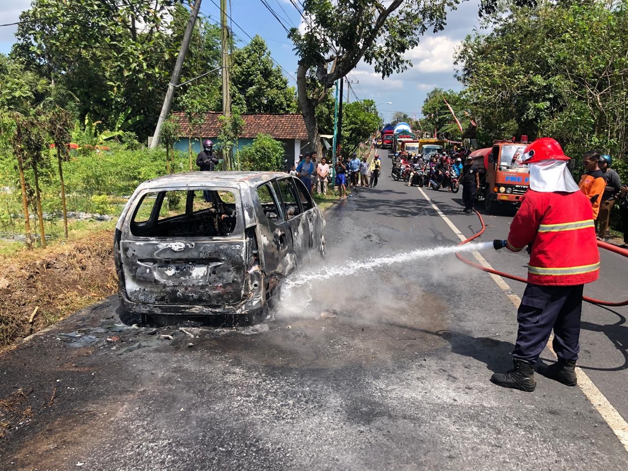 HANGUS: Anggota Damkarmat Sektor Bangorejo memadamkan mobil Daihatsu Xenia di jalan raya Desa Purwodadi, Kecamatan Gambiran Senin (12/8).