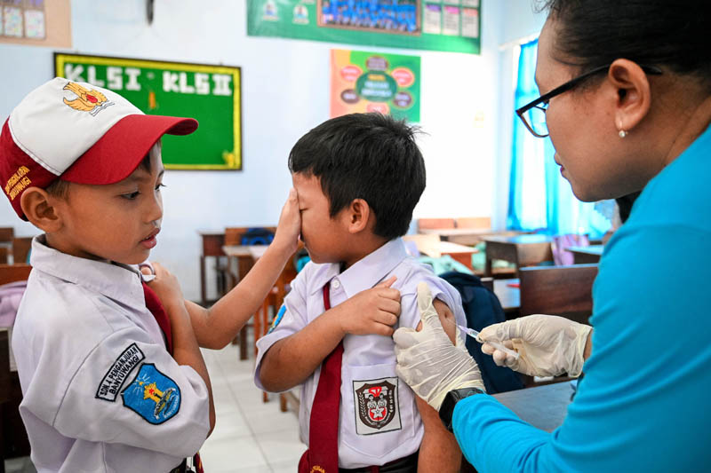 SALING BANTU: Salah satu siswa SDN 4 Penganjuran menutup mata temannya supaya tidak melihat jarum yang disuntikkan oleh petugas medis Selasa (3/9).