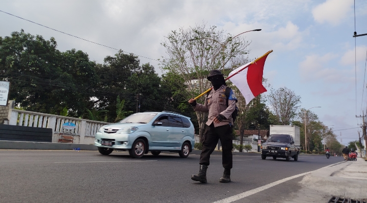 BAWA BENDERA: Anggota Polsek Wongsorejo Aipda Partika Budi Santoso berjalan kaki dari Polsek Wongsorejo menuju Polresta Banyuwangi, Kamis (26/9).