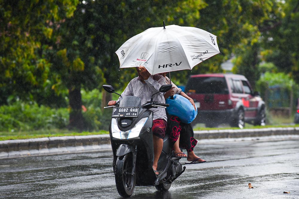 KURANG TEPAT: Warga menggunakan payung saat berkendara sepeda motor ketika hujan mengguyur.