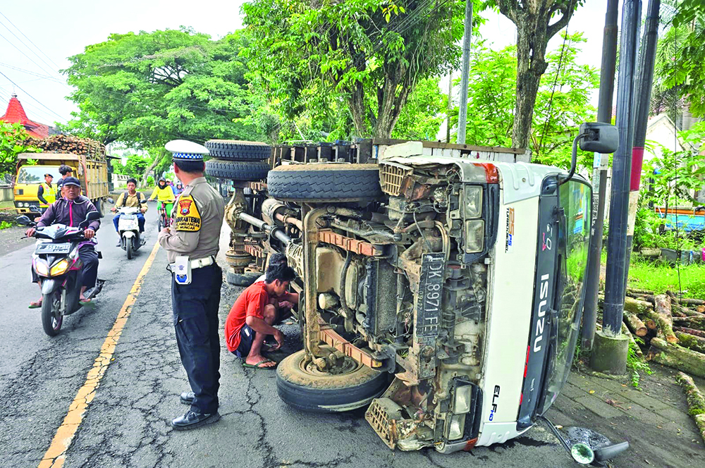 RODA LEPAS: Truk bermuatan kayu terguling di Jalan Brawijaya, Desa Kedungrejo, Kecamatan Muncar, Jumat (31/1).