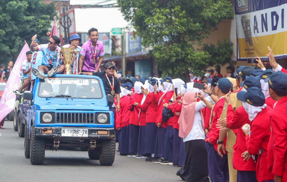 Pemain Persewangi Sandi Maulana (kacamata hitam), dan Muhammad Zaki Ali Sapari (baju ungu), bersama trofi juara 1 Liga 4 Jatim disambut meriah oleh para pelajar di Jalan Gajah Mada, Genteng, Senin (24